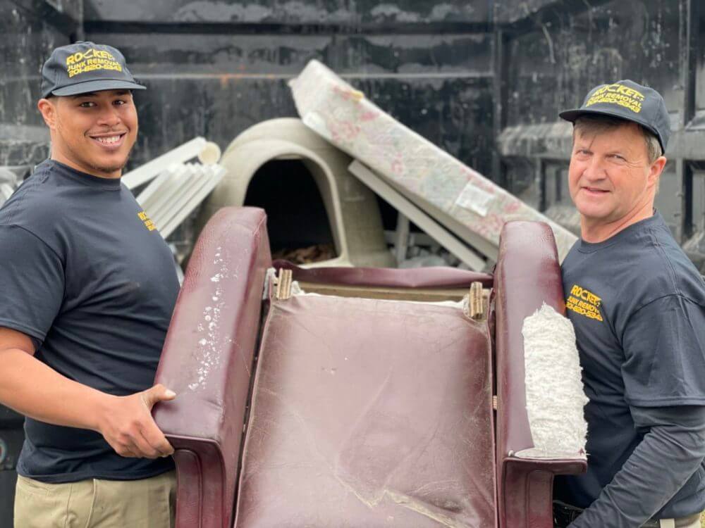 Smiling Rocket Junk Removal employees holding a couch